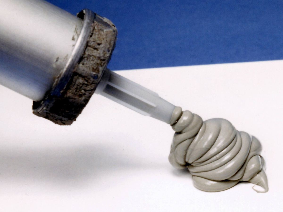 Gray caulk squeezed from the nozzle of a caulking gun
